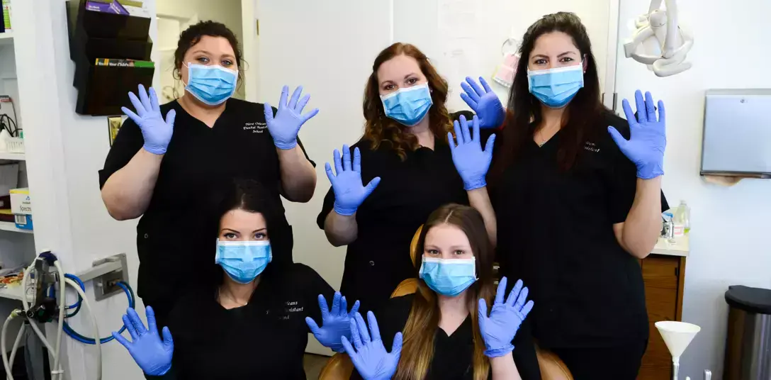 {{ school.name }} students posing for a group photo with gloves and masks on in dental office