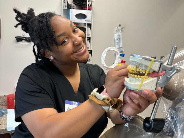 {{ school.name }} student posing with a dental mold for assistant training